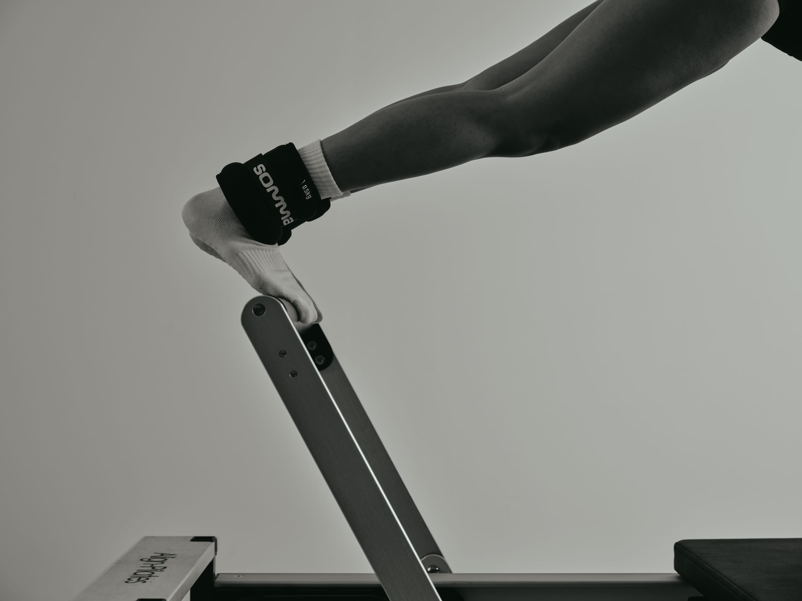 A leg wearing a somma ankle weight, extended onto a reformer bar